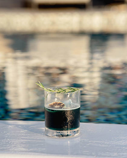 Grand Ambassador pool bar cocktail with ice, rosemary garnish, and poolside reflections