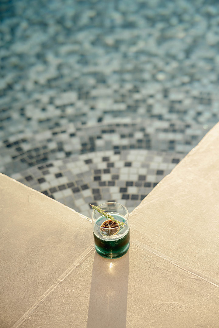 Grand Ambassador pool bar green cocktail with rosemary and citrus garnish by mosaic pool edge