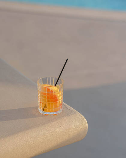 Grand Ambassador pool bar orange cocktail with straw on poolside edge