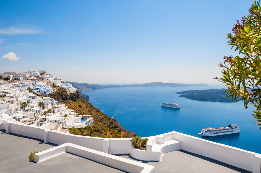 Santorini cliffside village with whitewashed buildings, cruise ships in the caldera, and bright blue sky