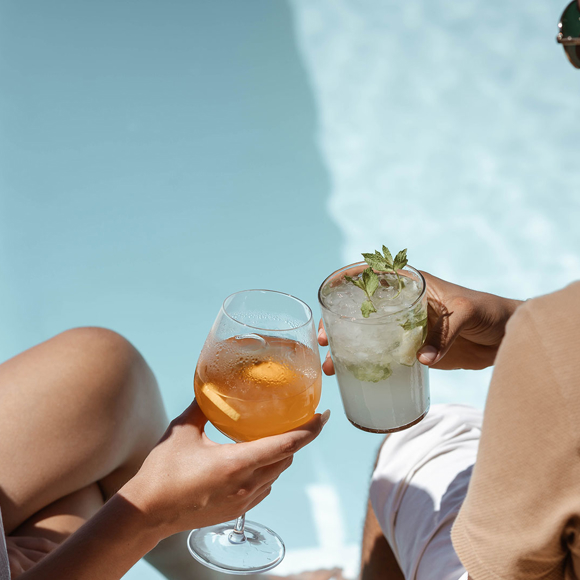 Two guests toasting drinks beside infinity pool at Grand Ambassador hotel