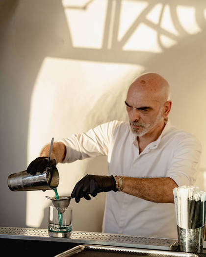 Grand Ambassador pool bar bartender pouring blue cocktail into a glass through a strainer at sunset