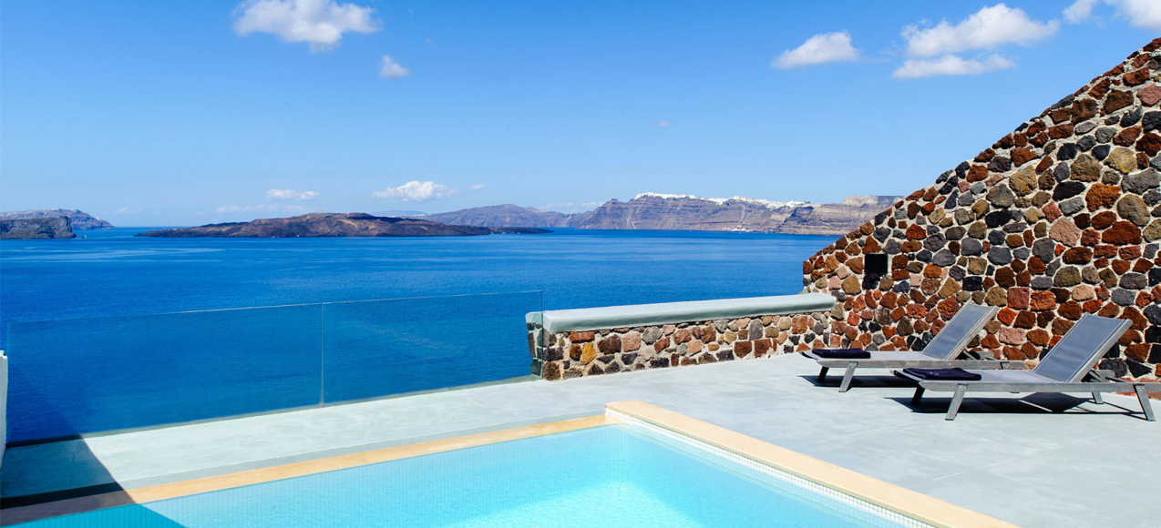 Poolside terrace with lounge chairs overlooking calm blue sea and distant islands under a bright sky