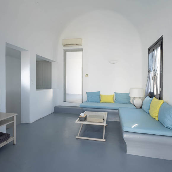 Grand Ambassador Santorini Serenity Two Bedroom Suite spacious living area with built-in blue sofas, yellow accent pillows, and minimalist decor