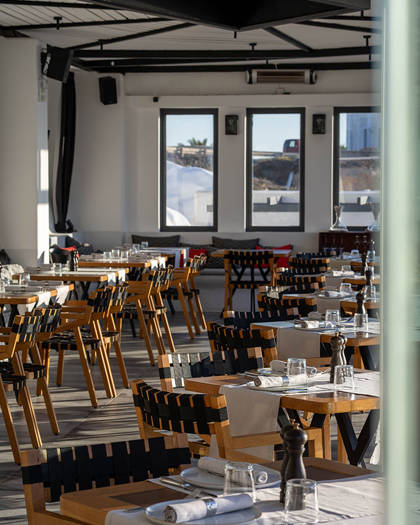 Grand Ambassador Dione restaurant indoor dining room with wooden chairs, set tables, and large windows