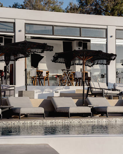 Grand Ambassador Dione restaurant poolside lounge area with sunbeds, umbrellas, and glass facade