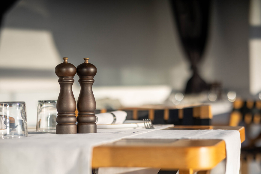 Grand Ambassador Dione restaurant table close-up with wooden pepper mills and glassware in sunlit dining area