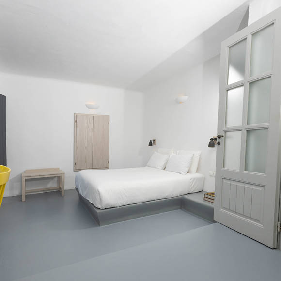 Grand Ambassador Santorini Serenity Two Bedroom Suite bedroom with double bed, desk, yellow chairs, and minimalist Cycladic decor