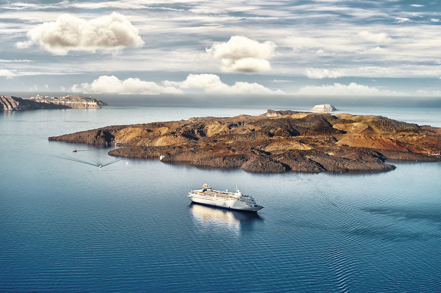 Santorini volcanic island with cruise ship in calm blue waters under partly cloudy sky